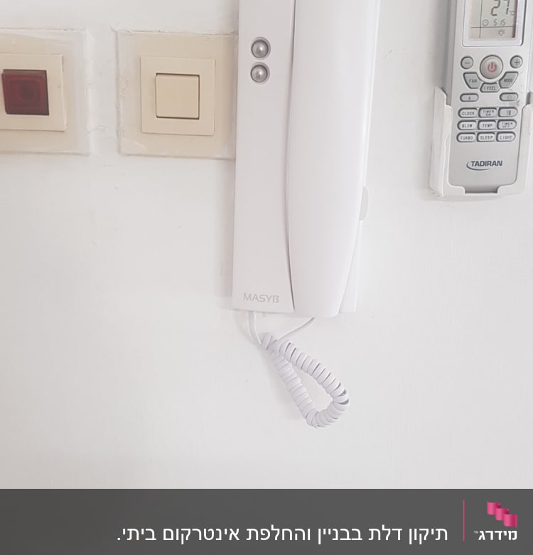 אינטרקום לבן עם שפופרת תלויה על הקיר